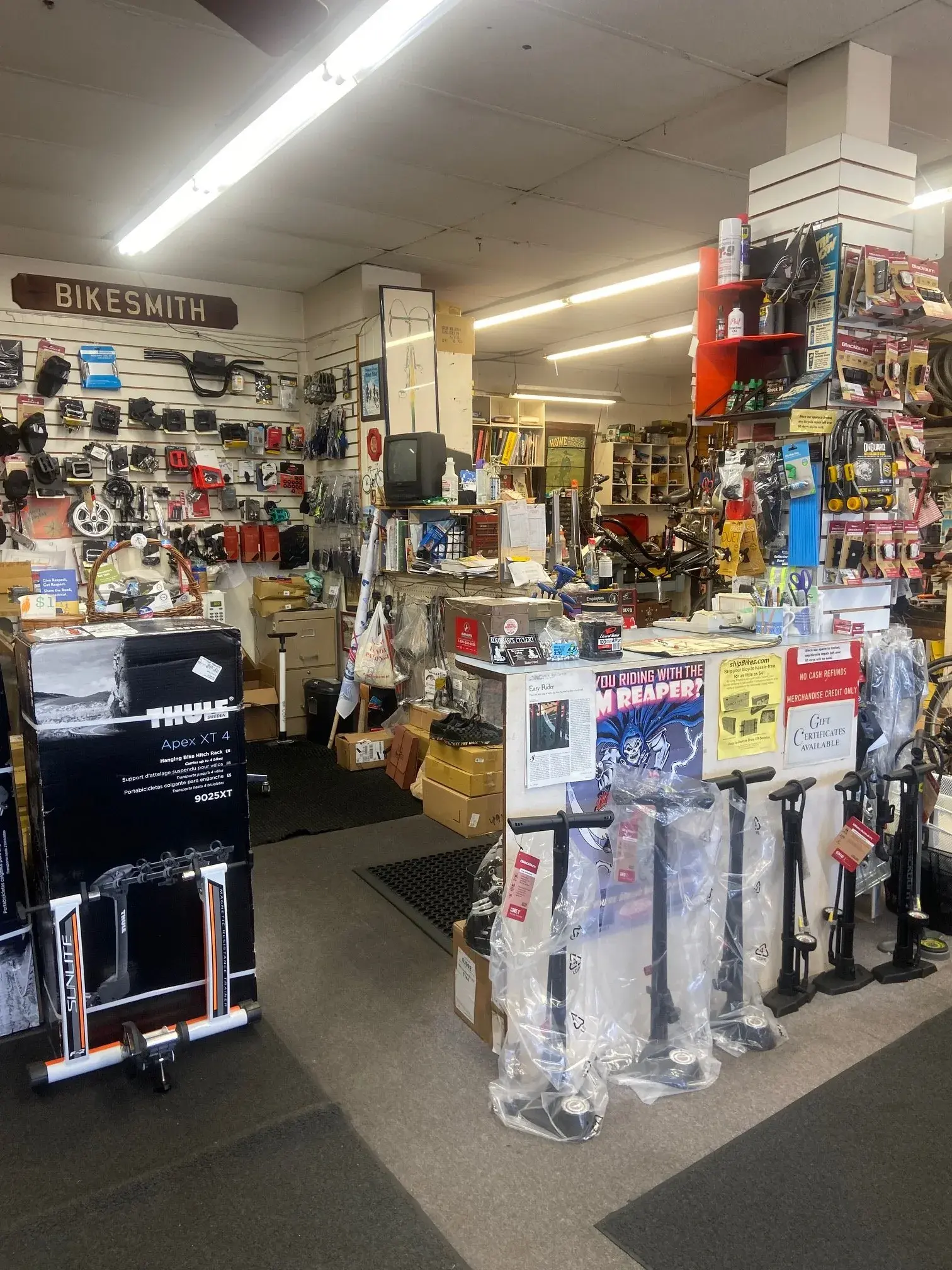 The parts wall and service counter under the shop's carved BIKESMITH sign, with floor pumps, locks and accessories