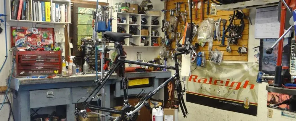 A bicycle in the repair stand at the workbench, beside the shop's Raleigh Bicycles banner and tool board