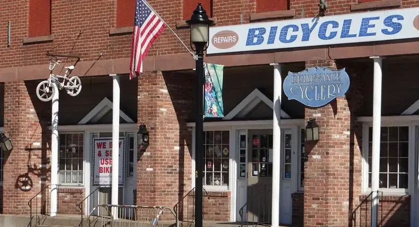Renaissance Cyclery's brick storefront on West Main Street, with its BICYCLES and REPAIRS signs, the Renaissance Cyclery hanging sign and an American flag